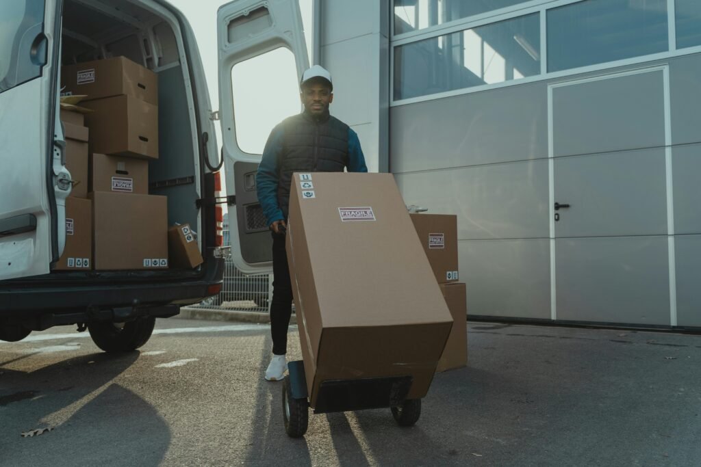 Delivery man with trolley unloading boxes from a van outside a warehouse.