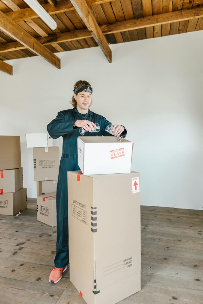 Man sealing moving boxes in a bright industrial setting. Ideal for relocation and logistics themes.